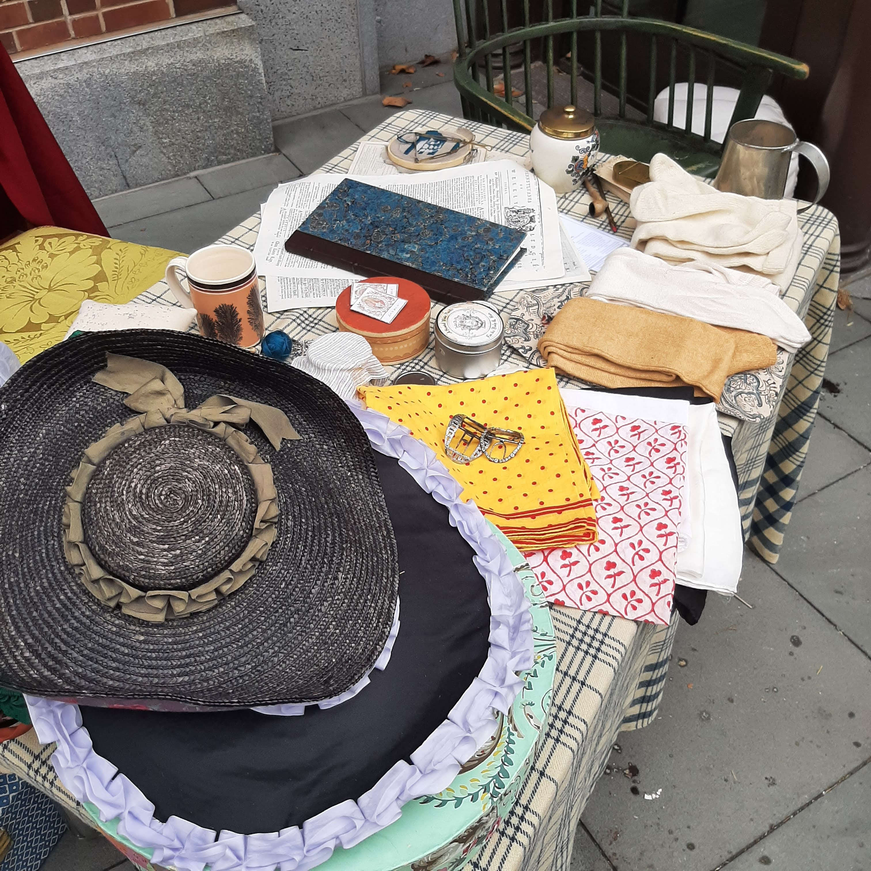 a stack of 18th century hats and patterned handkerchiefs sit on a check blanket