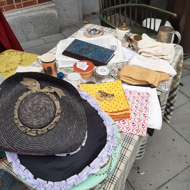 a stack of 18th century hats and patterned handkerchiefs sit on a check blanket