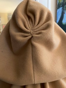 the pleated back of a cloak hood made of butterscotch colored wool